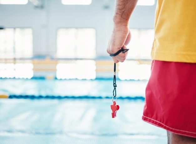 Lifeguard And Swim Instructor standing at pool with whistle